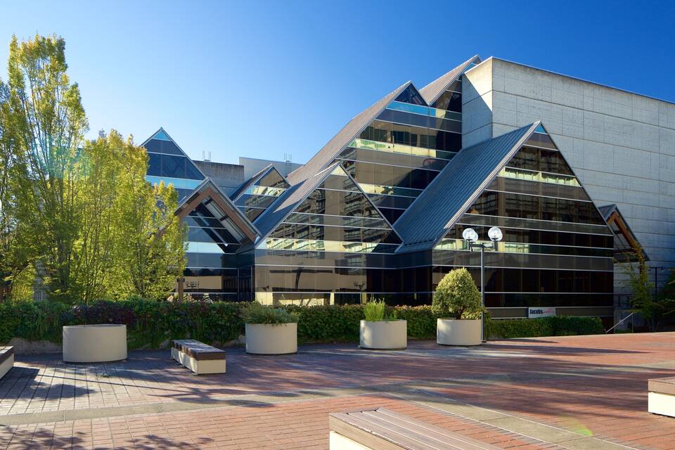 A modern building with a unique angular design, surrounded by a landscaped area with benches and trees.