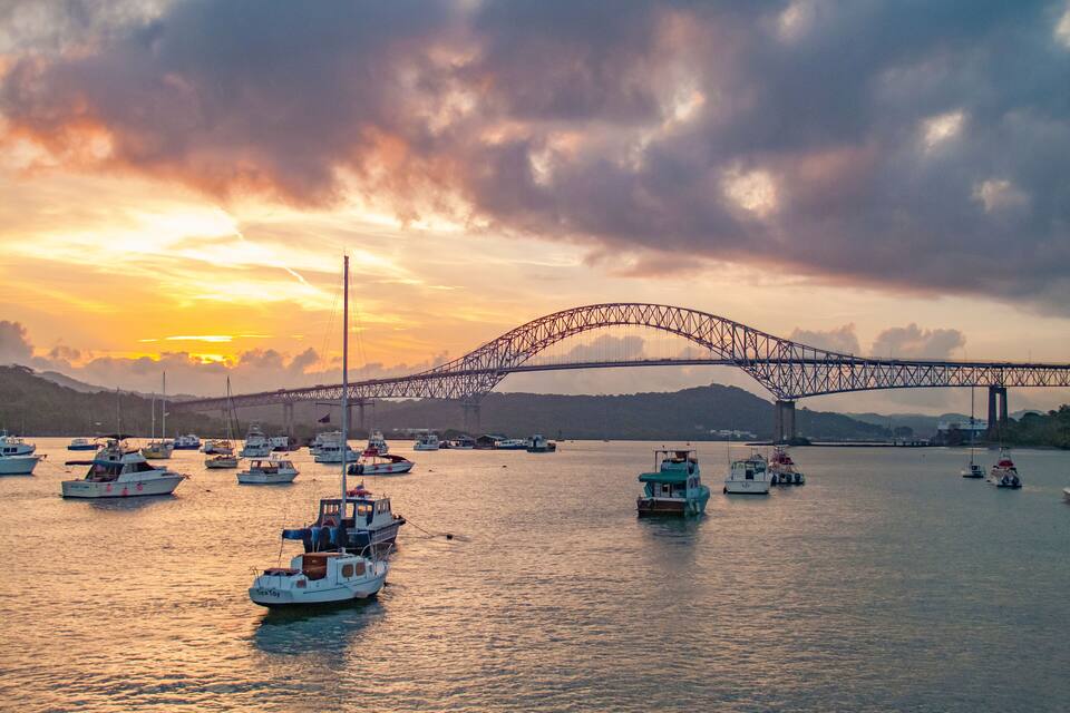 Tramonto su un corpo d'acqua con un ponte e diverse imbarcazioni.