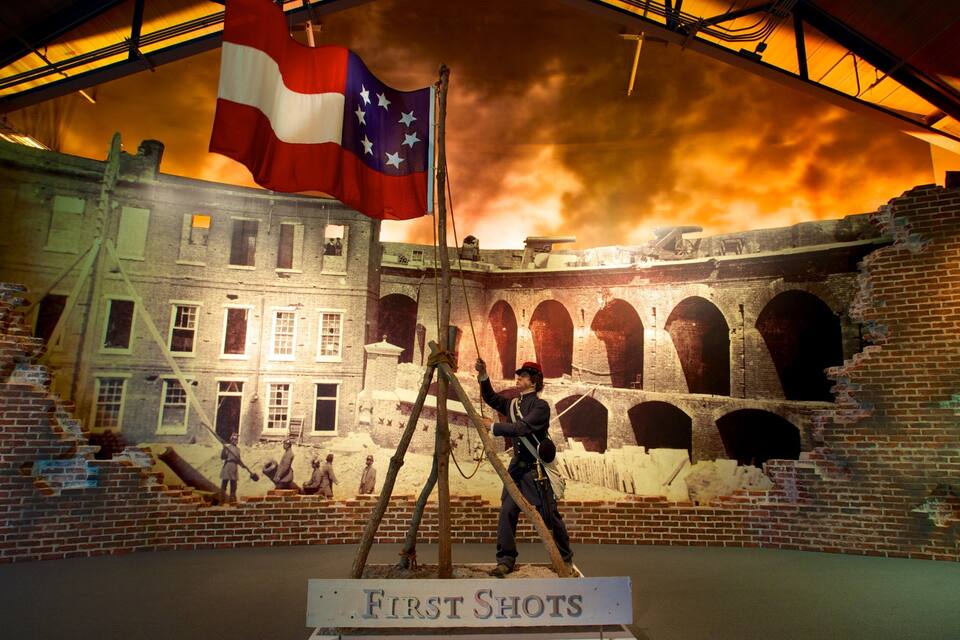 Un diorama historique représentant une scène avec une figure en uniforme, un drapeau et une pancarte indiquant « Premiers tirs ».
