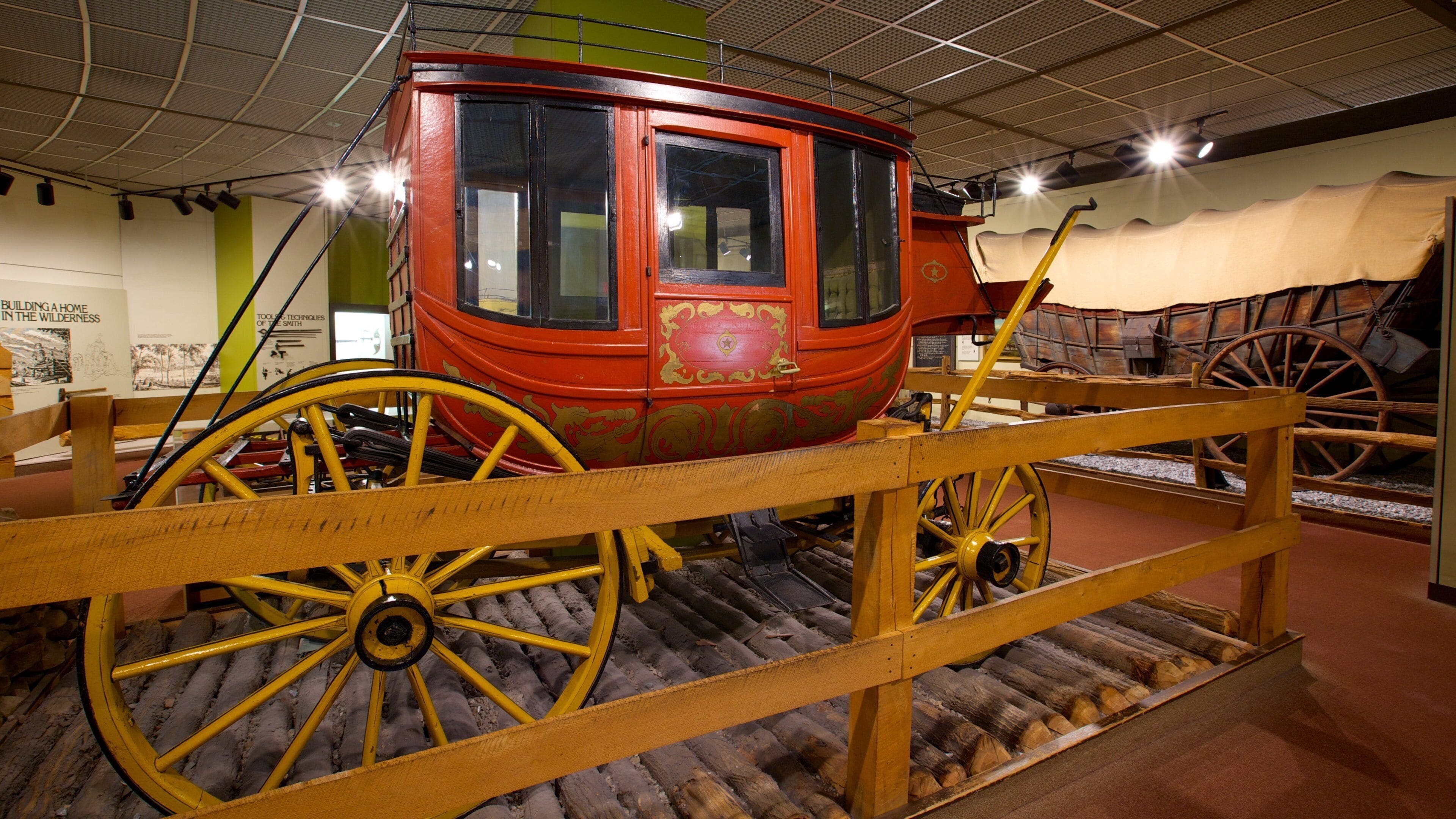 A red covered wagon with yellow wheels on display in a museum.