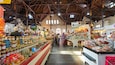 Un marché couvert où divers étals proposent des produits alimentaires, comme du pain, des pâtisseries et des condiments.