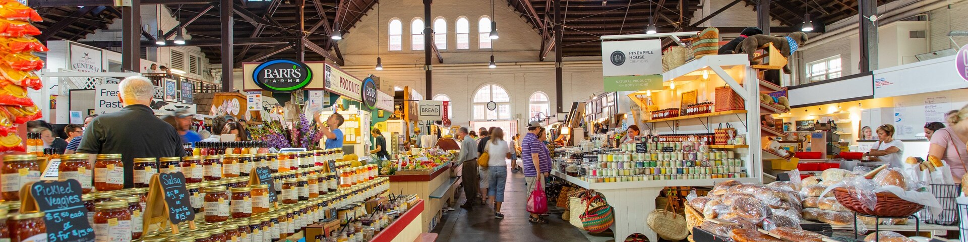 Mercado interno com vários quiosques vendendo produtos alimentícios como pão, doces e temperos.
