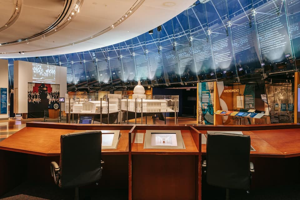 Una exhibición de museo con un amplio muro de vidrio que muestra texto y una maqueta del Capitolio de los Estados Unidos.