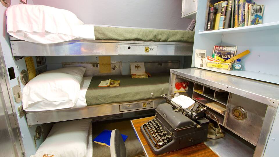 A compact, metallic room with bunk beds, a typewriter, and a shelf with books.