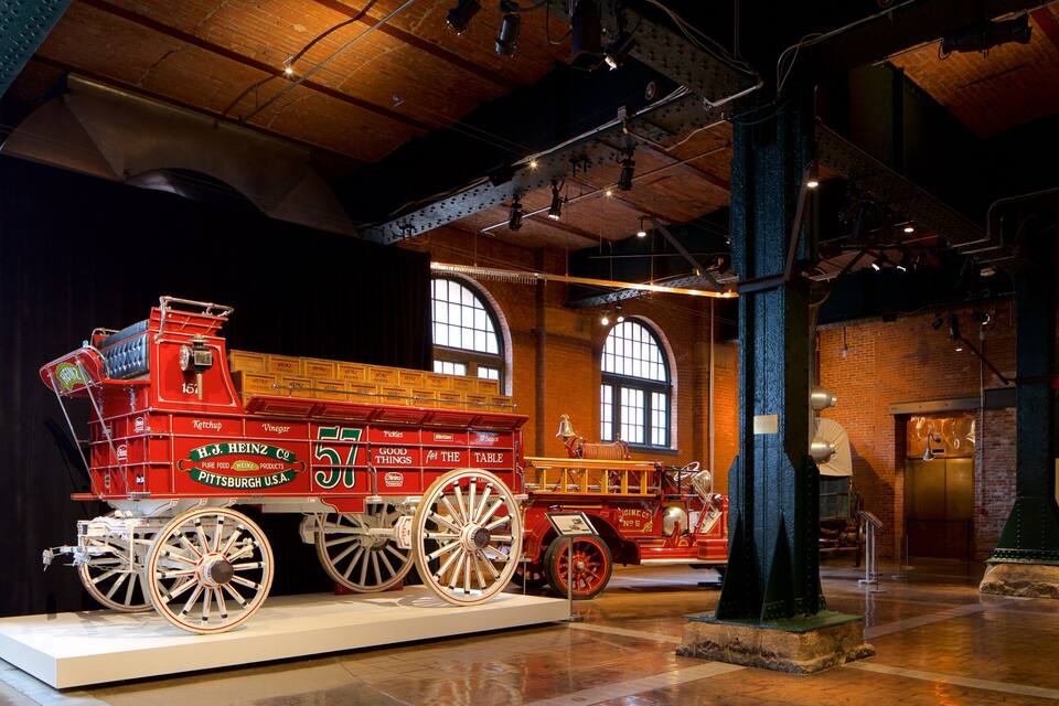 Een oude brandweerwagen in een museum met grote ramen en bakstenen muren.