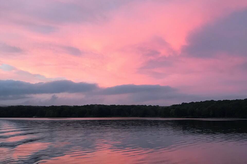 A calm lake at sunset with pink and purple clouds reflected in the water.