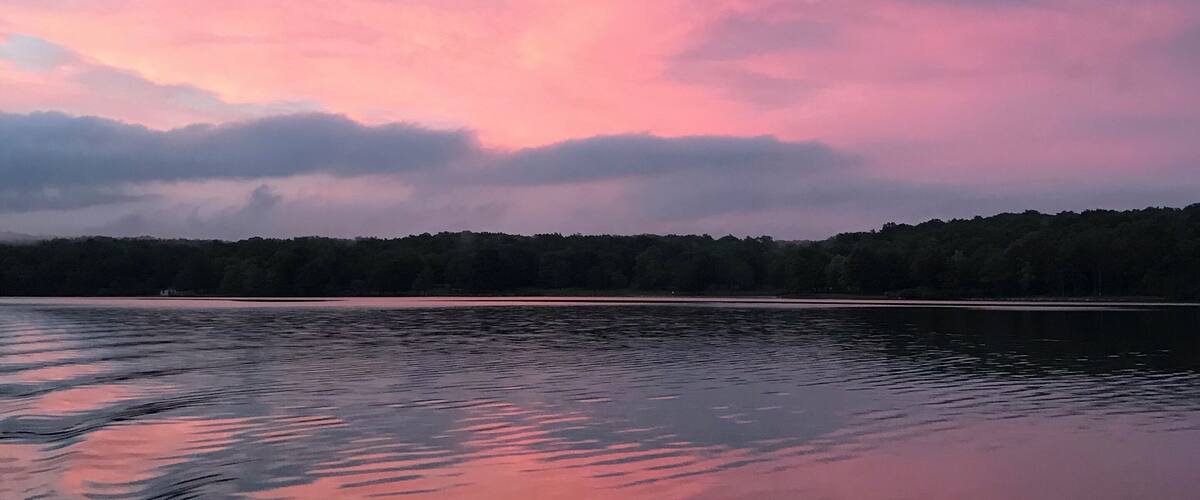 A calm lake at sunset with pink and purple clouds reflected in the water.