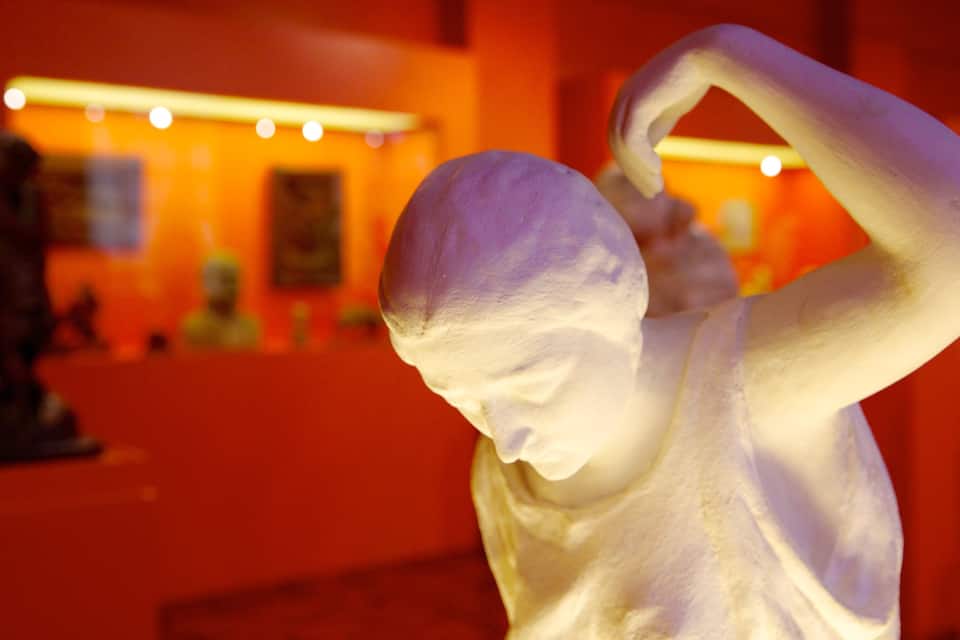 A white sculpture in a museum with a red background and other sculptures in the background.