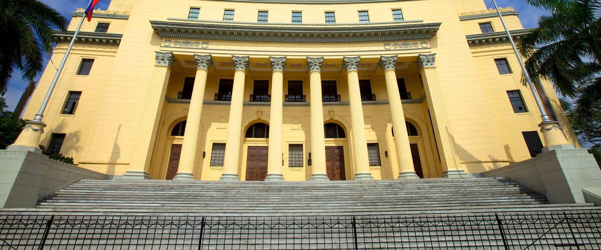 A grand yellow building with columns, a staircase, and flags.