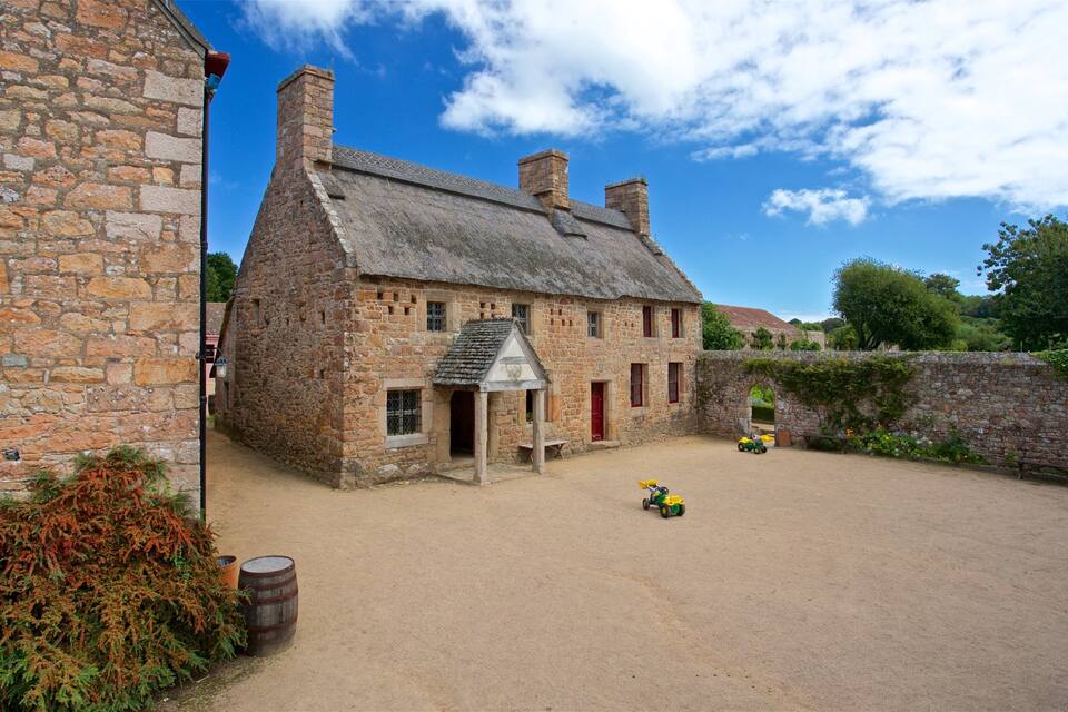 A stone building with a thatched roof, a dirt courtyard, and a toy car.