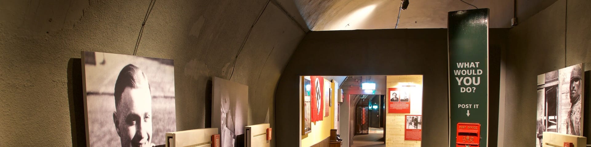 A hallway with historical exhibits, including a large poster with a man and text, and a red post office box.