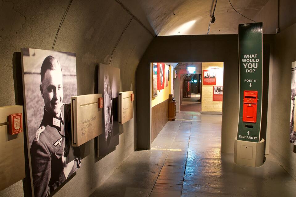 Un pasillo con exhibiciones históricas, incluyendo un cartel grande con un hombre y texto, y un buzón rojo de correos.