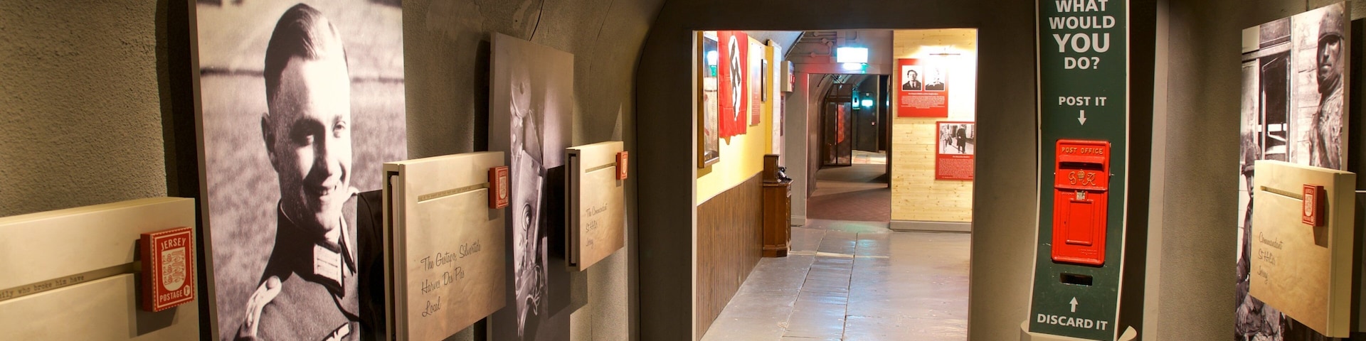 Um corredor com exposições históricas, incluindo um cartaz grande com um homem e texto, e um caixa de correio vermelho.