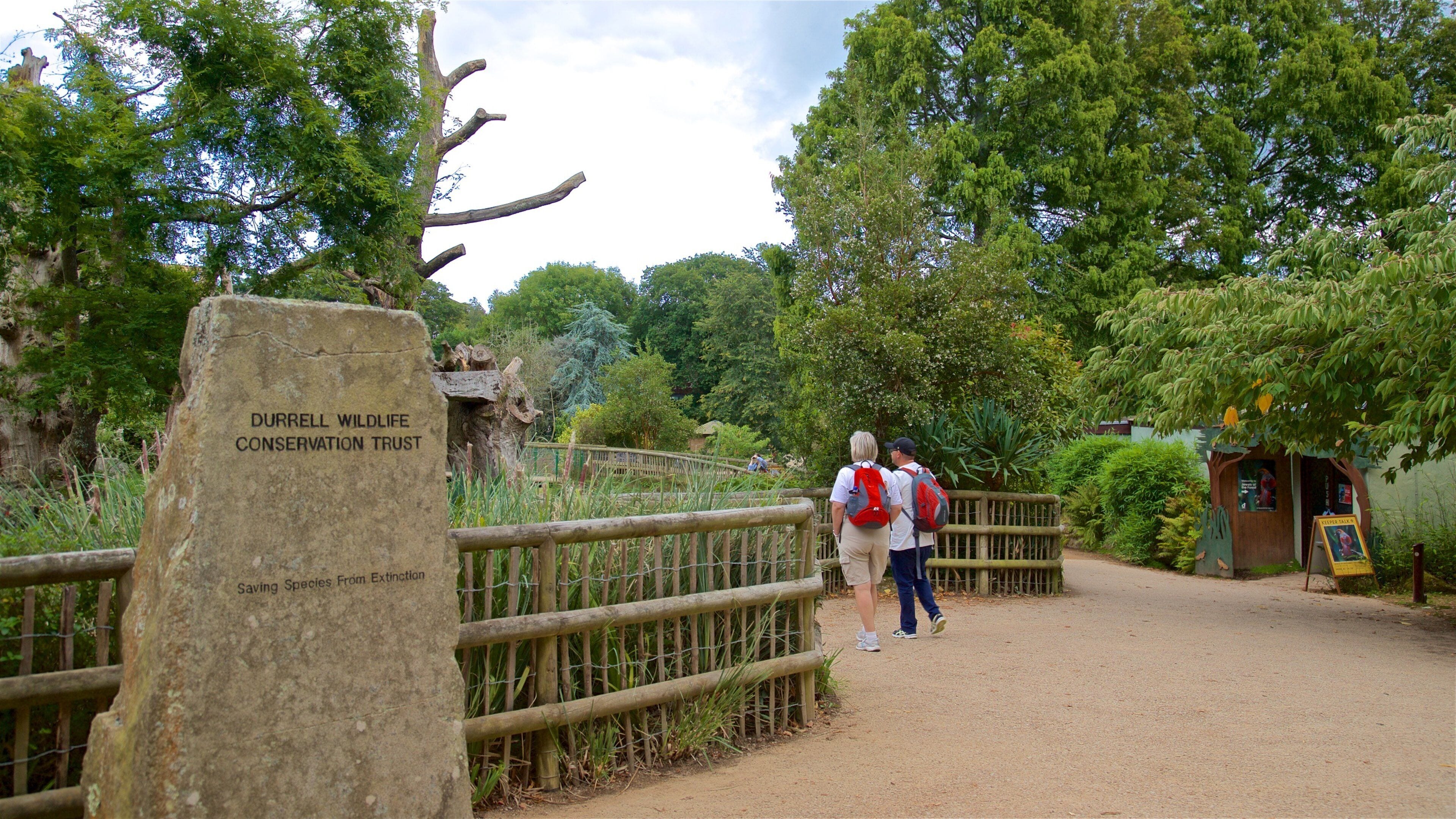 A wooden bridge, a sign for Durrell Wildlife Conservation Trust, and a small building with a signboard.