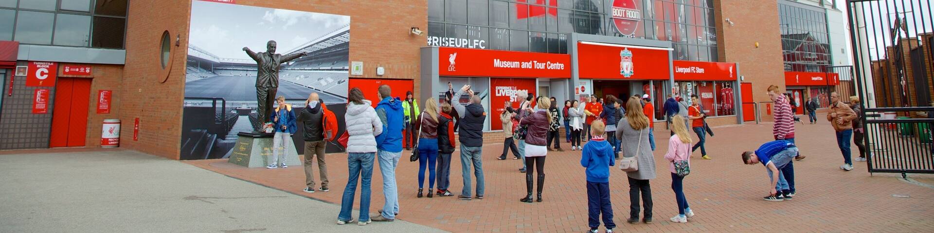 A stadium with a large glass facade, red signage, and a crowd of people.