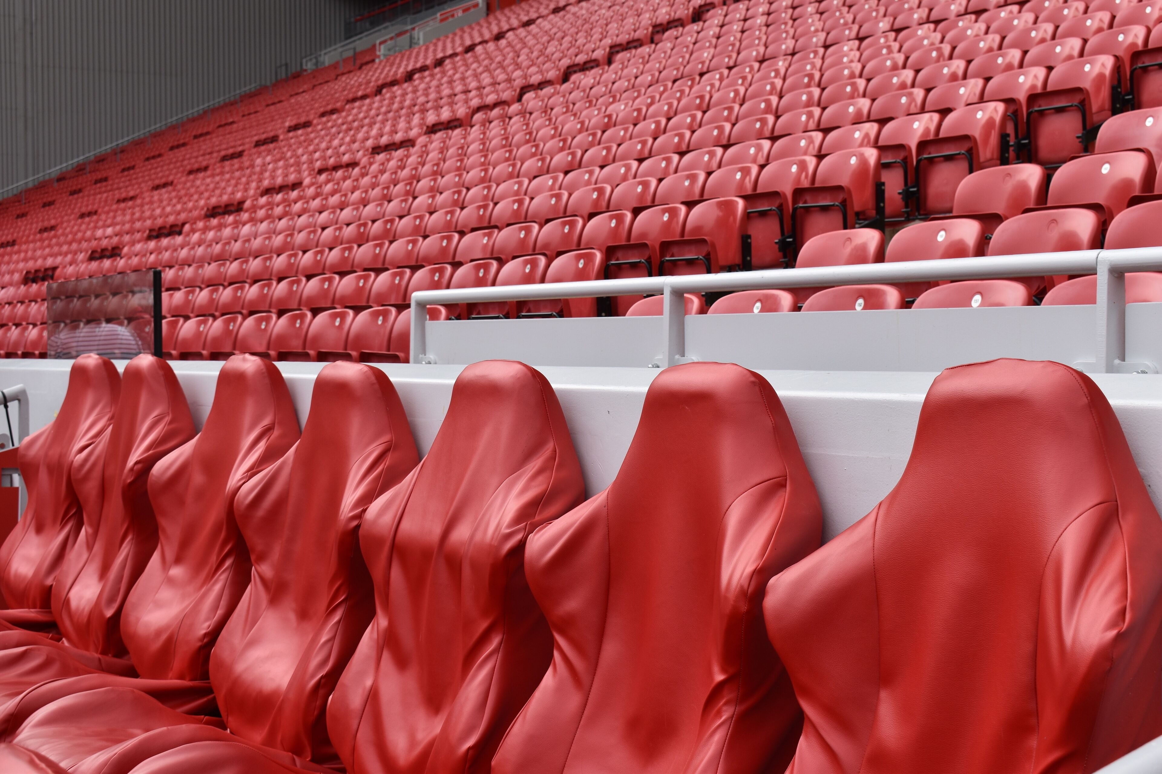 Empty red leather and plastic seats. In stadium seating back seats are placed higher than seats in front so occupants of back seats have less views blocked by those forward. Liverpool, UK