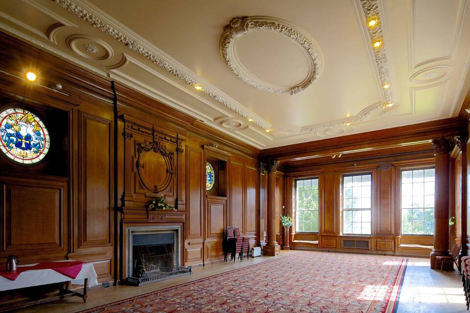 A grand room with ornate wood paneling, a large stained glass window, and a fireplace.