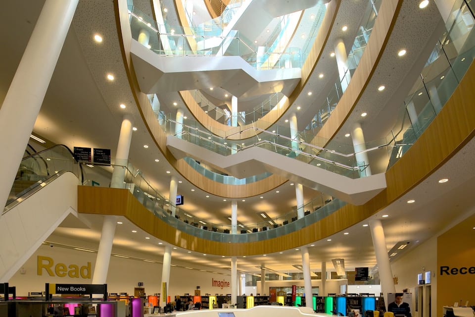 Een meerlaags atrium met glazen balustrades, boekenkasten en borden met 'Read' en 'Receptie'.