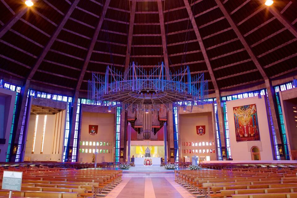 Ample interior d'una catedral amb un sostre alt, finestres de vitralls i un altar central.