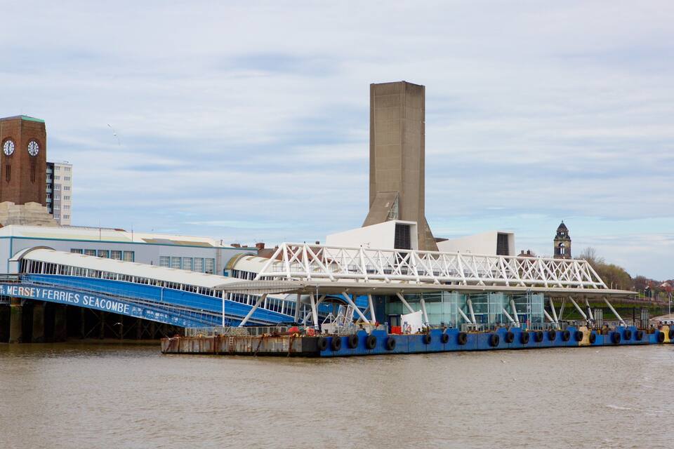 A ferry dock with a bridge, a tall building with a clock, and a river.