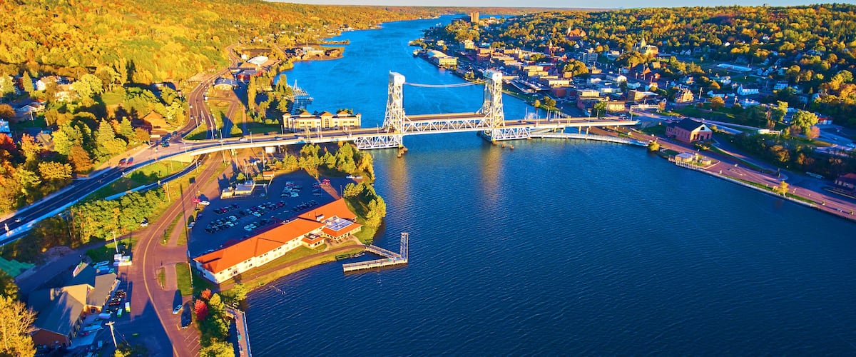 A river with a bridge, a town on the opposite bank, and surrounding hills.