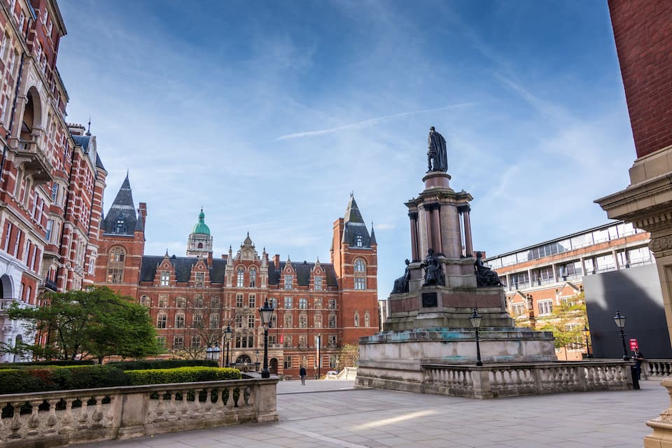 Um edifício histórico com arquitetura em tijolos vermelhos, uma estátua e um céu azul límpido.