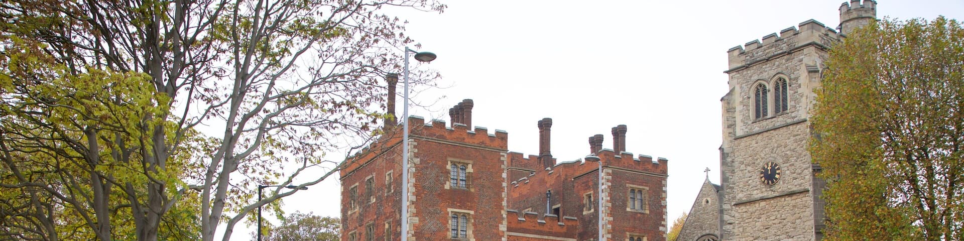 A historic building with a clock tower, surrounded by trees and a well-maintained garden.