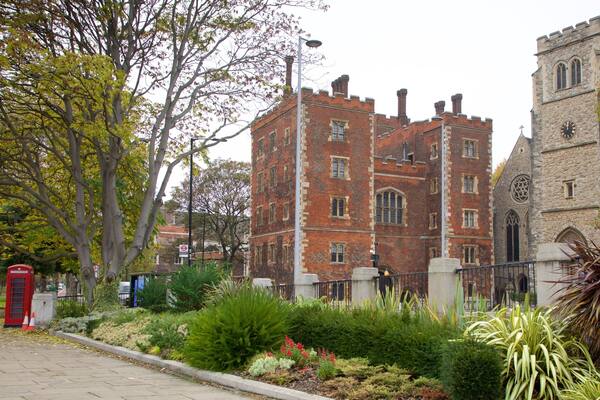 A historic building with a clock tower, surrounded by trees and a well-maintained garden.