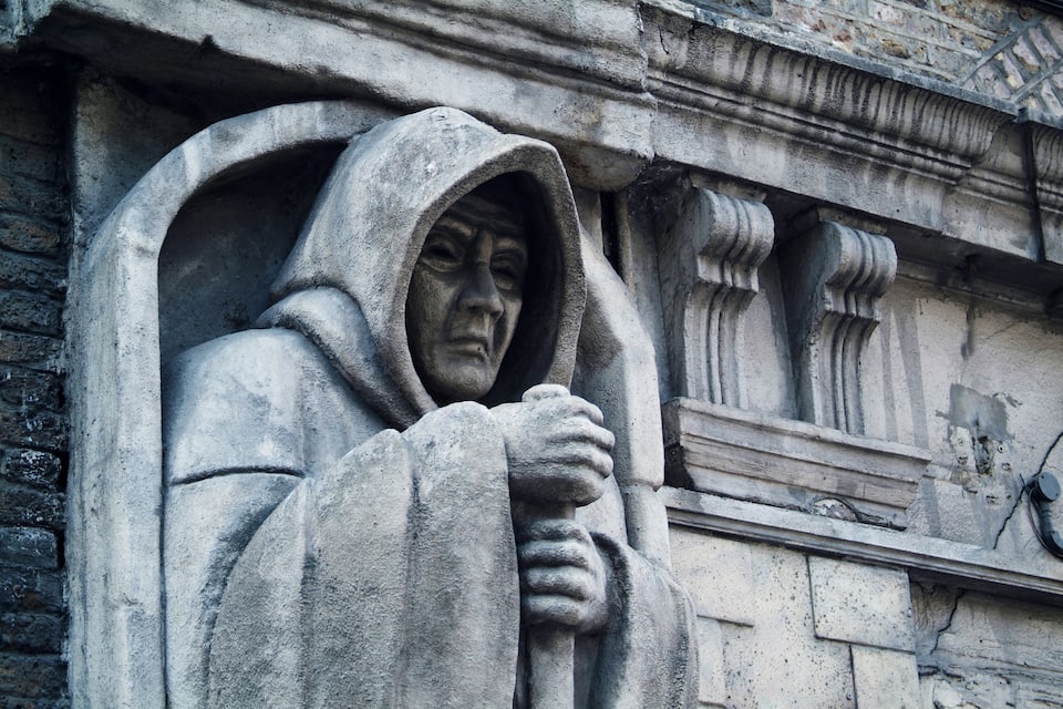 Een stenen beeldhouwwerk van een figuur met kap en samengevouwen handen.