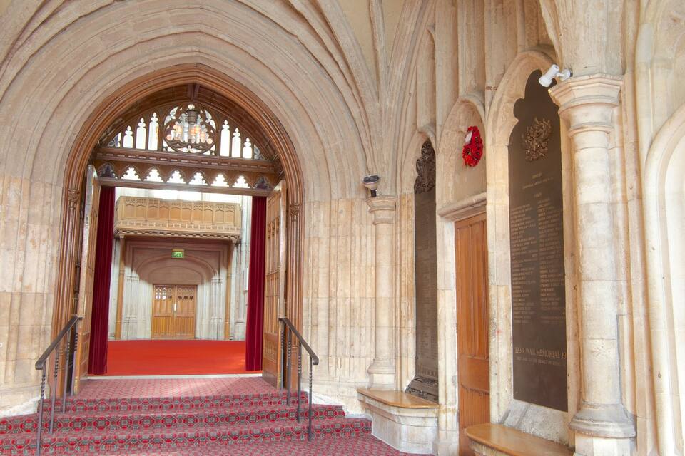 A grand stone staircase leading to a red-carpeted area with a stained glass window above.