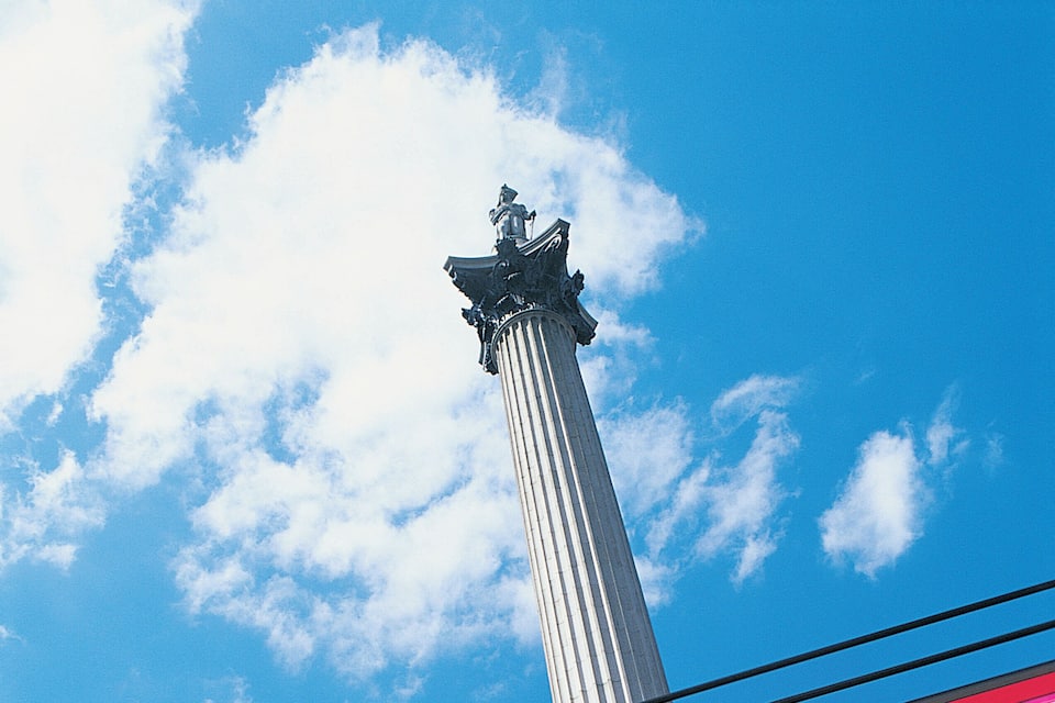 A red train passing by a tall, slender monument against a blue sky with clouds.