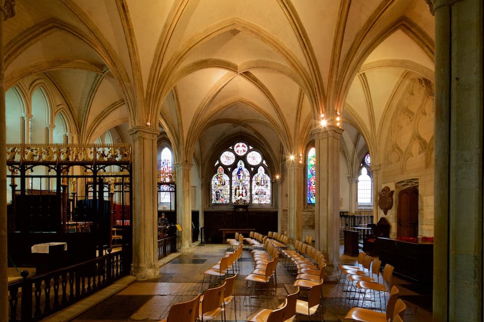 A church interior with arched ceilings, stained glass windows, and rows of chairs.