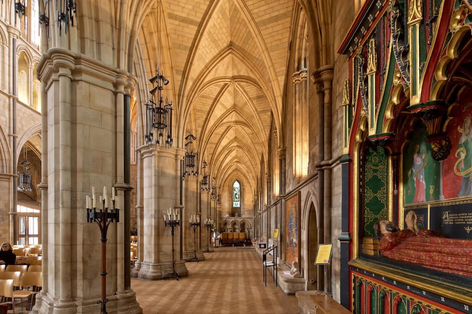 A cathedral interior with arched ceilings, stone columns, and a stained glass window.