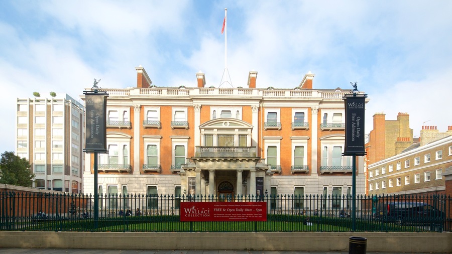 Un edificio histórico con un estandarte rojo, un asta de bandera y una valla verde.
