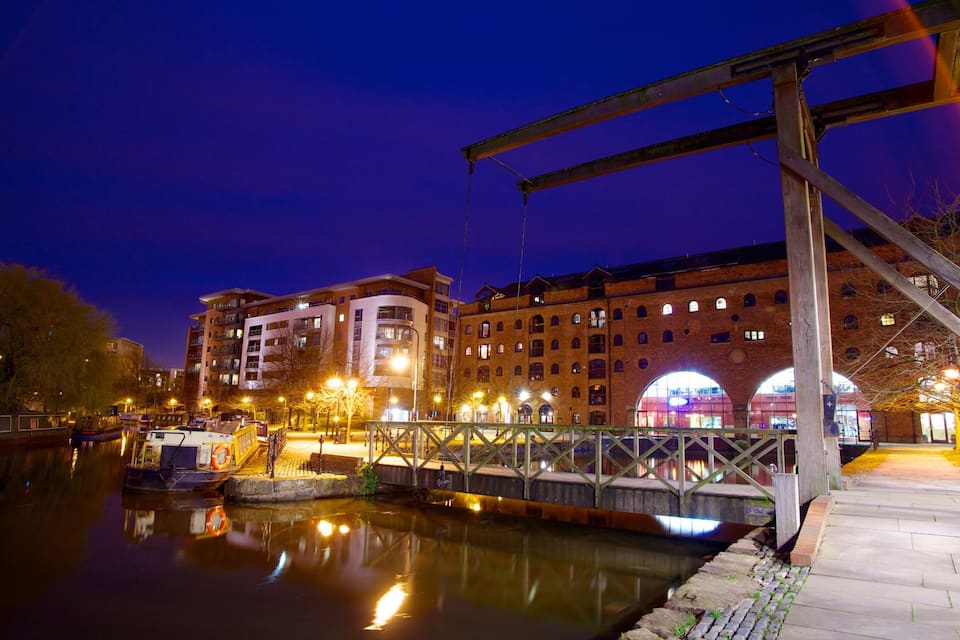 Una escena nocturna a la orilla del río con un puente, edificios y barcos.