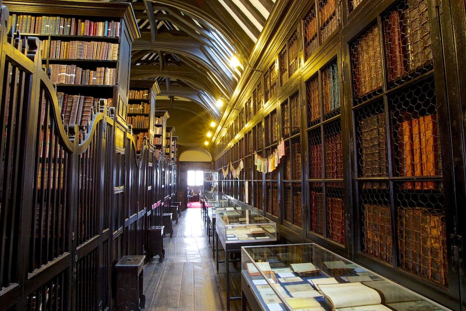 Een bibliotheek met hoge boekenkasten, een houten vloer en een glazen vitrine met boeken.