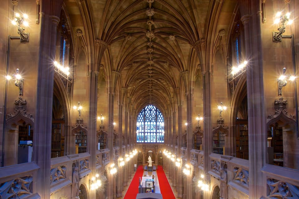 L’intérieur d’une cathédrale, avec un tapis rouge, de hauts plafonds en arc de cercle et une grande fenêtre à vitraux au fond.