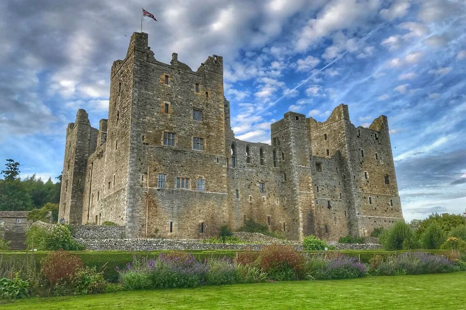 Un château historique doté de nombreuses tours et surmonté d’un drapeau, entouré de jardins bien entretenus.