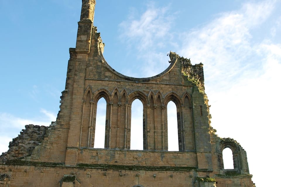 The ruins of a medieval stone building with arched windows and a tall tower.