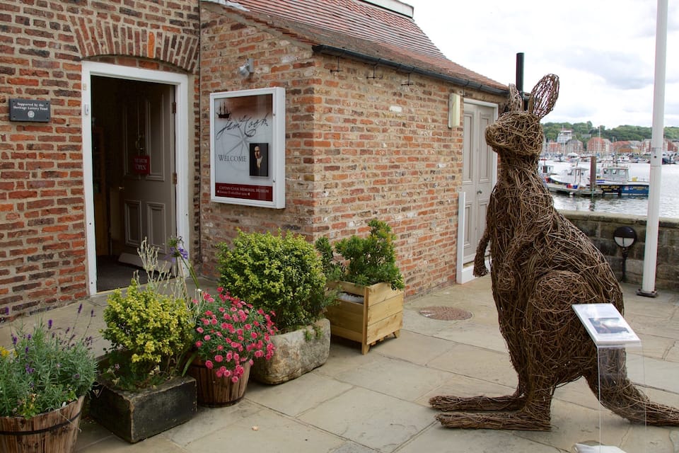 A brick building with a sign for the Carlaw Cook Memorial Museum. There are potted plants and a large kangaroo sculpture outside.