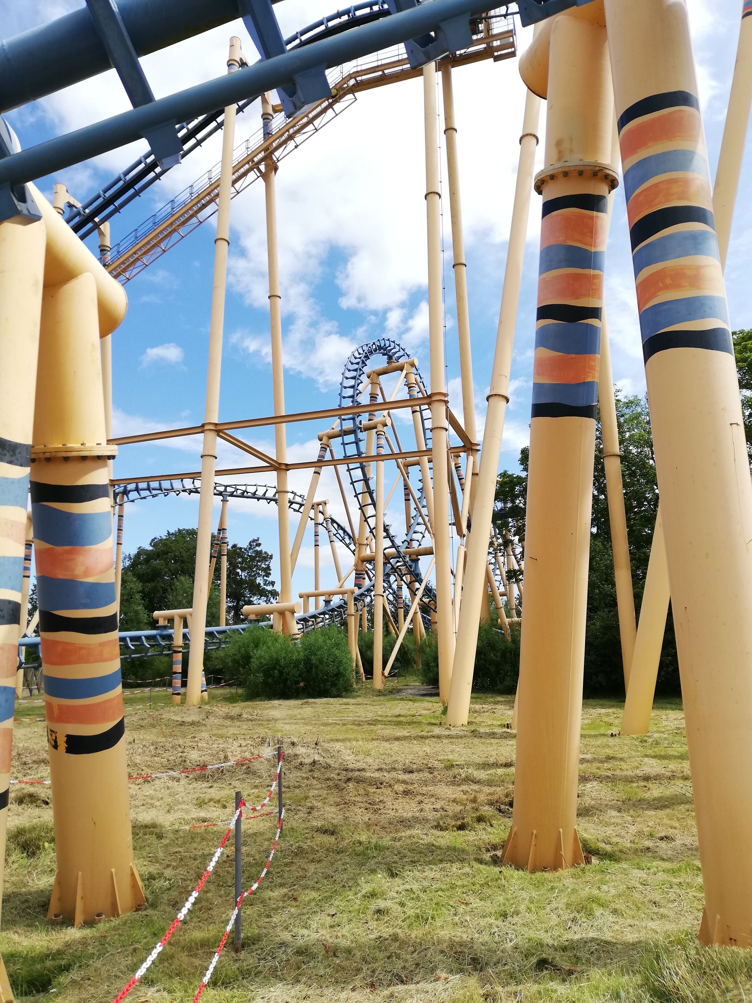 A roller coaster with a wooden track and a blue loop, surrounded by tall, striped support columns.