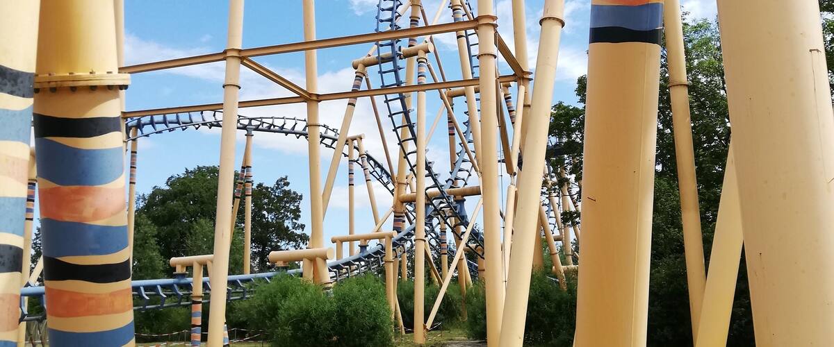 A roller coaster with a wooden track and a blue loop, surrounded by tall, striped support columns.