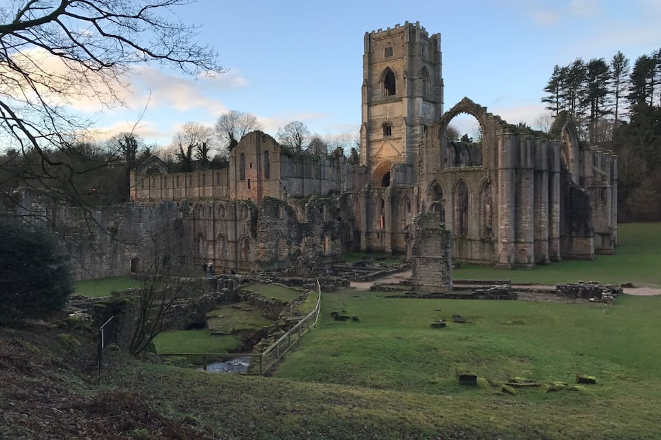 Un ancien château de pierre, doté d’une haute tour, entouré de ruines et d’un champ verdoyant.