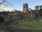 An ancient stone castle with a tall tower, surrounded by ruins and a grassy field.