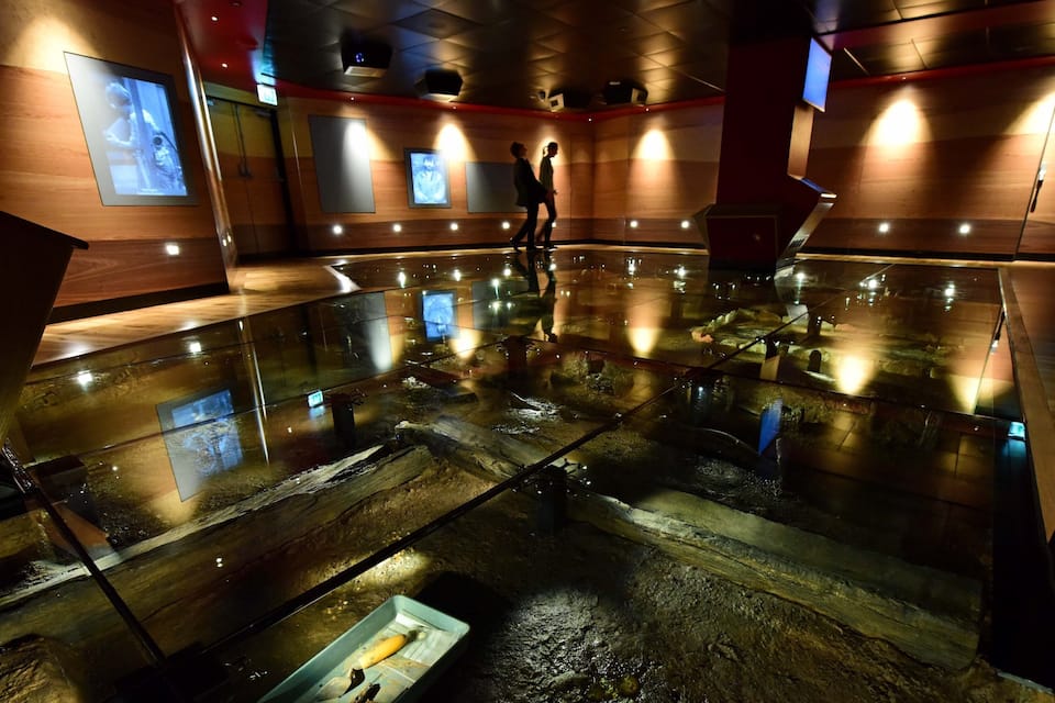 A dimly lit room with a reflective floor, wooden walls, and a person standing near a display case.