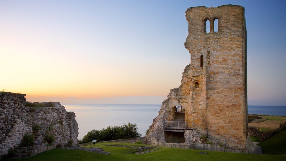 A historic stone tower with arched windows, overlooking a calm sea at sunset.
