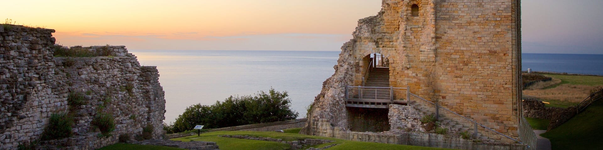 A historic stone tower with arched windows, overlooking a calm sea at sunset.