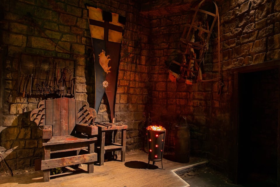 A rustic stone room with a wooden bench, a fireplace, and a ladder.