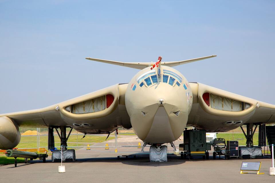 Un avión militar estacionado en una pista con cielo despejado al fondo.