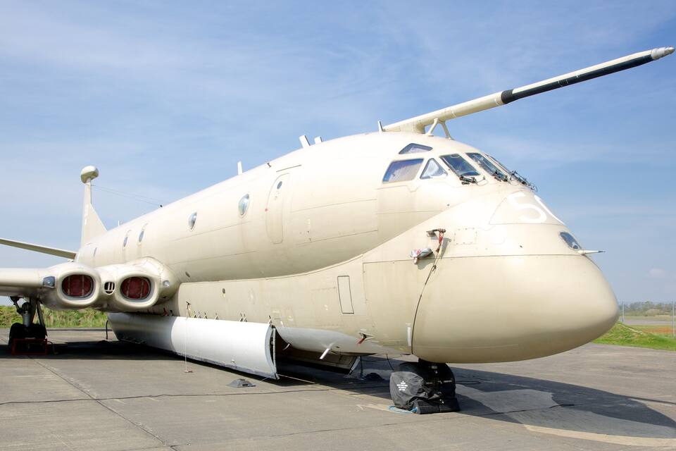 Uma aeronave militar em um pátio de estacionamento, com céu claro ao fundo.